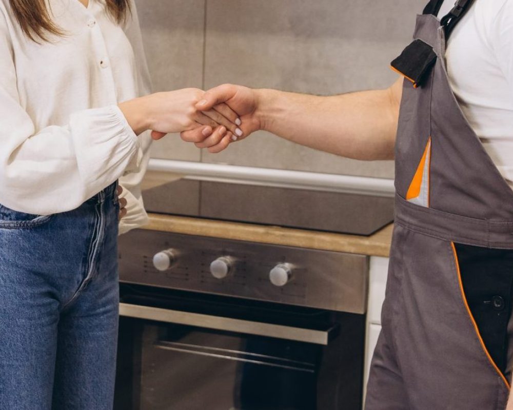 Plumber shaking hands with customer in kitchen after finishing work, home repair service concept